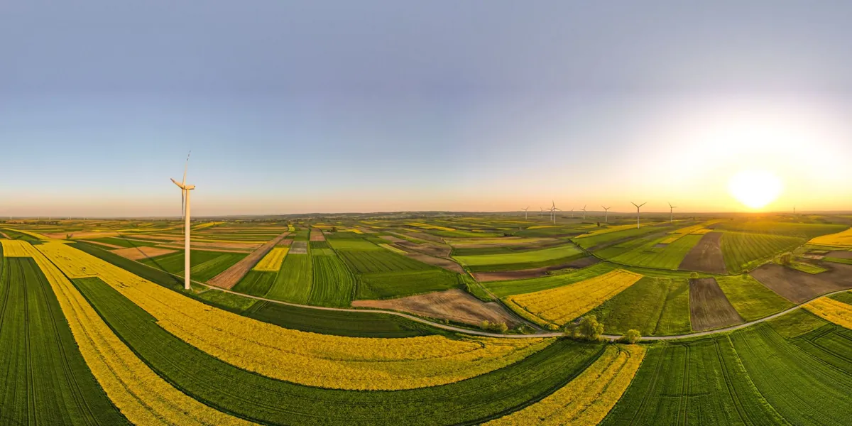 Aerial view of wind turbines amidst colorful farmland in Kosina, Poland during sunset.