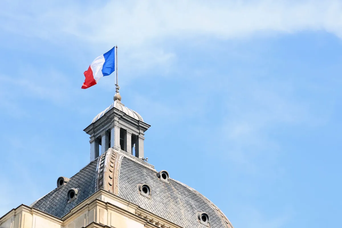 The French flag waves atop the dome of historic architecture in Paris, France.